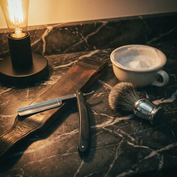 Straight razor, leather strop and shaving brush on a marble counter